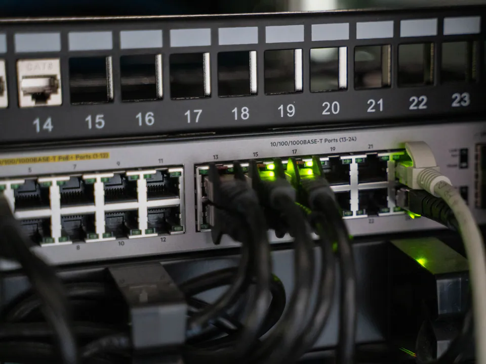 Patch cables plugged into a network switch under a numbered patch panel, its port lights glowing green