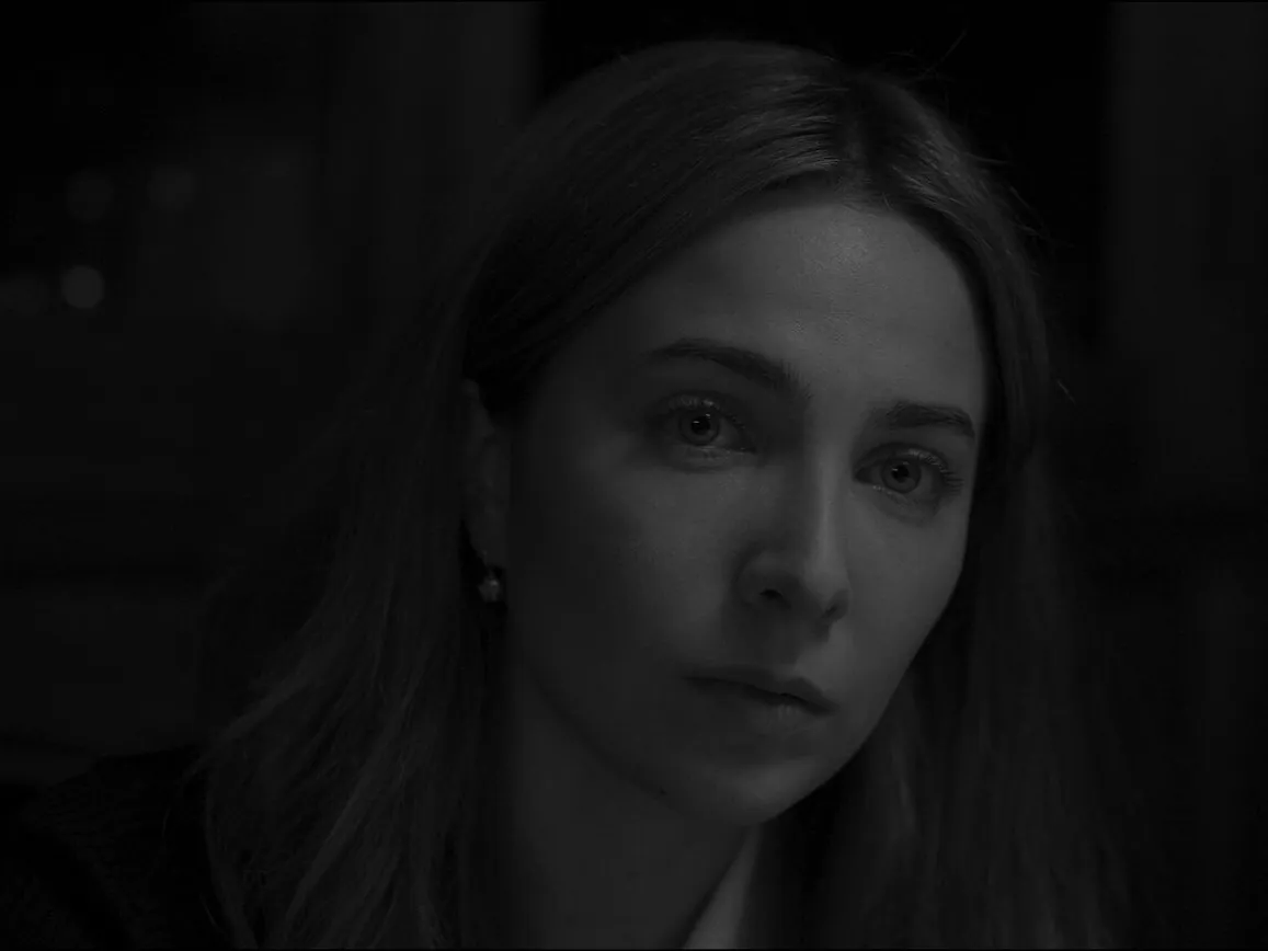 Film still from Exsanguination, in black and white: a woman in close-up, lit from one side in a dark room
