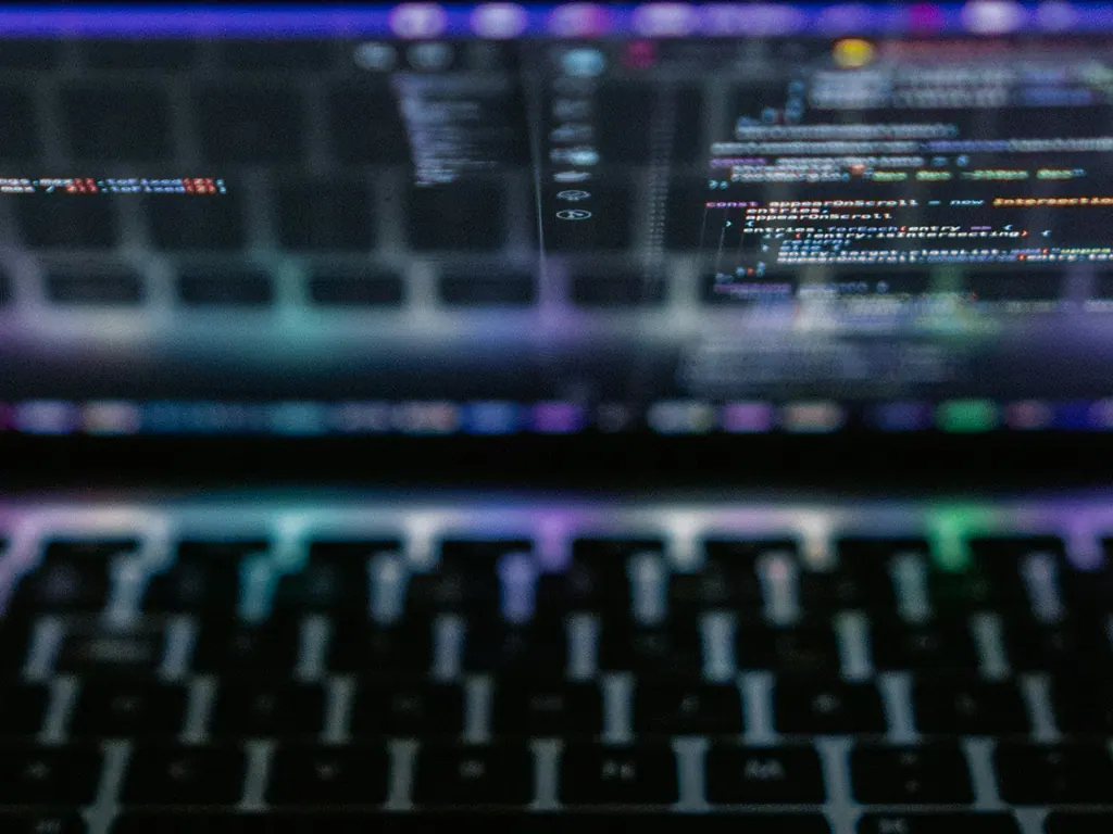 Code on a laptop screen, blurred out of focus above the keyboard